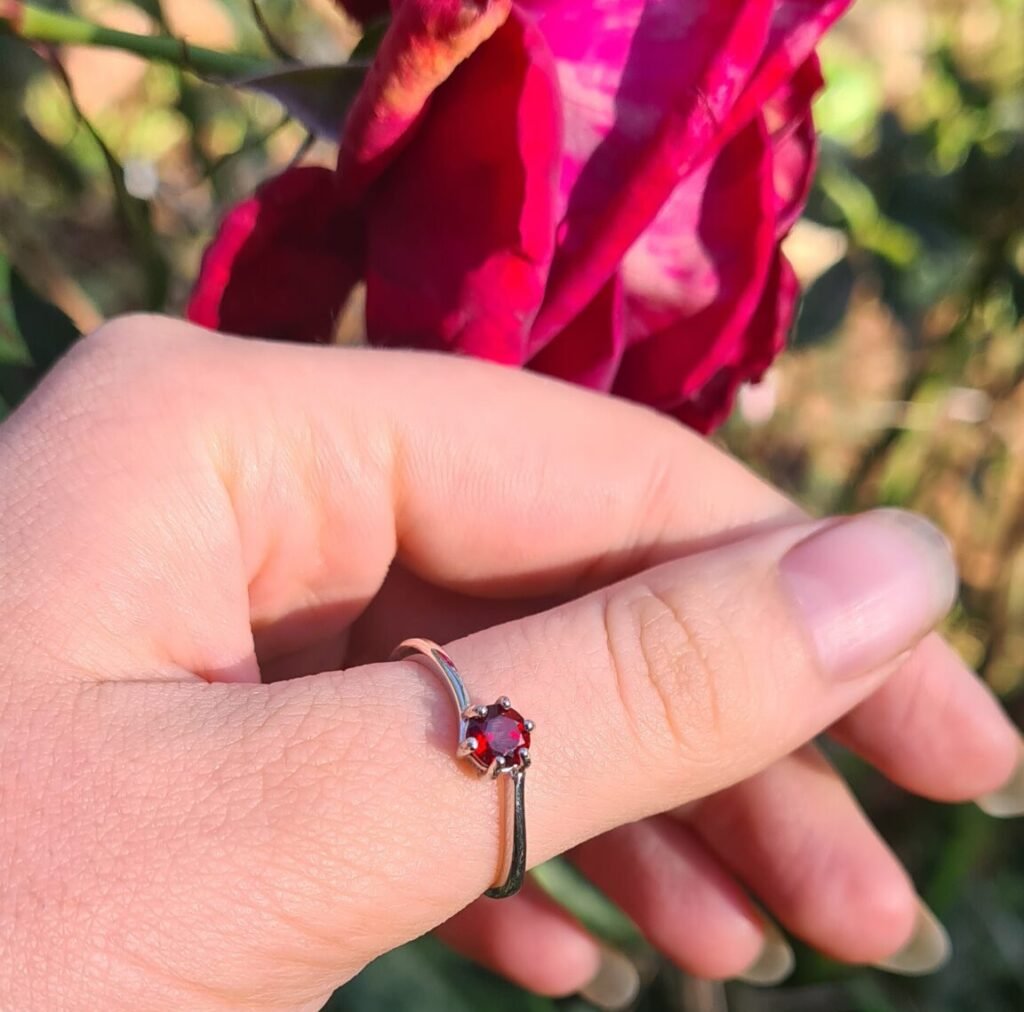 Jemagic garnet ring on thumb with red rose in the background