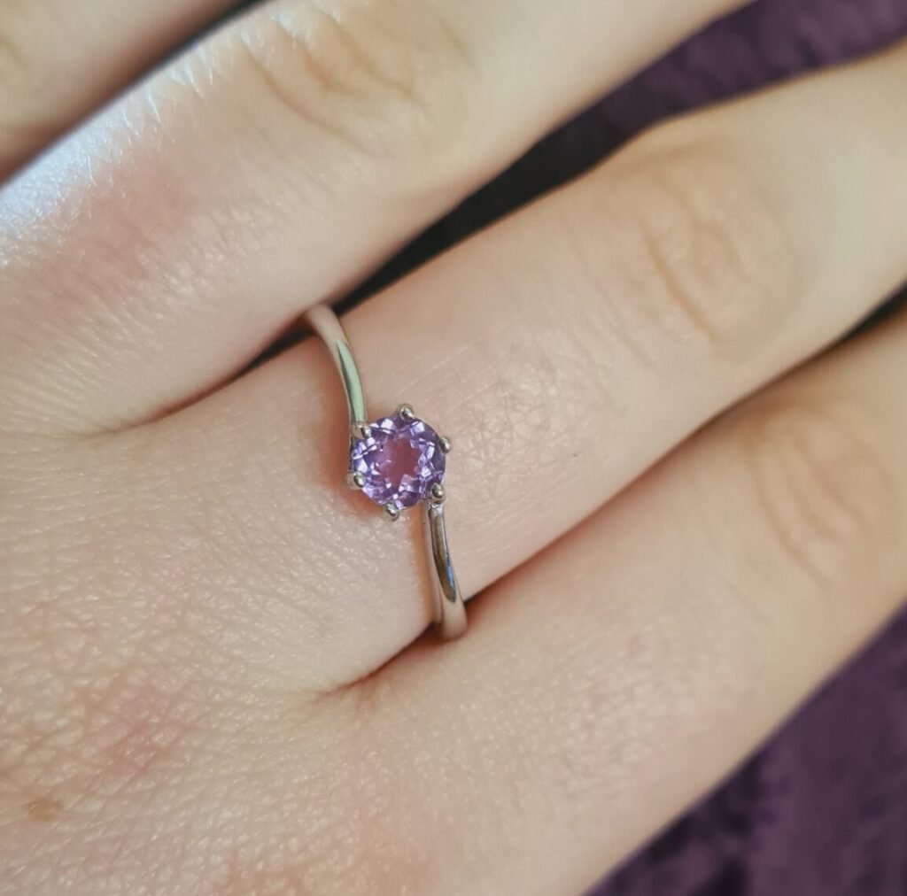 Jemagic amethyst ring being worn on middle finger with fluffy purple fabric background